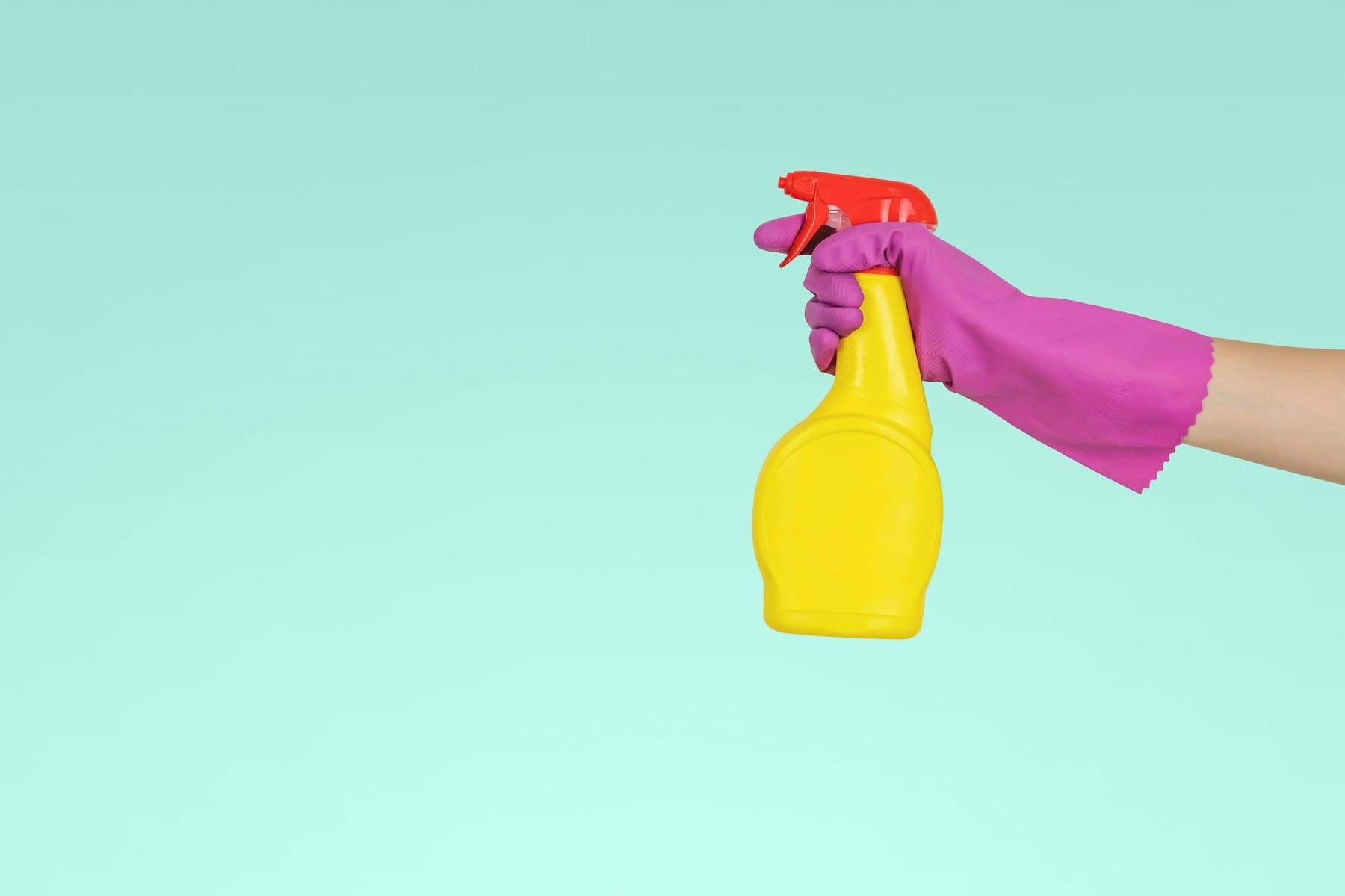 A gloved hand holding a spray bottle of cleaning solution